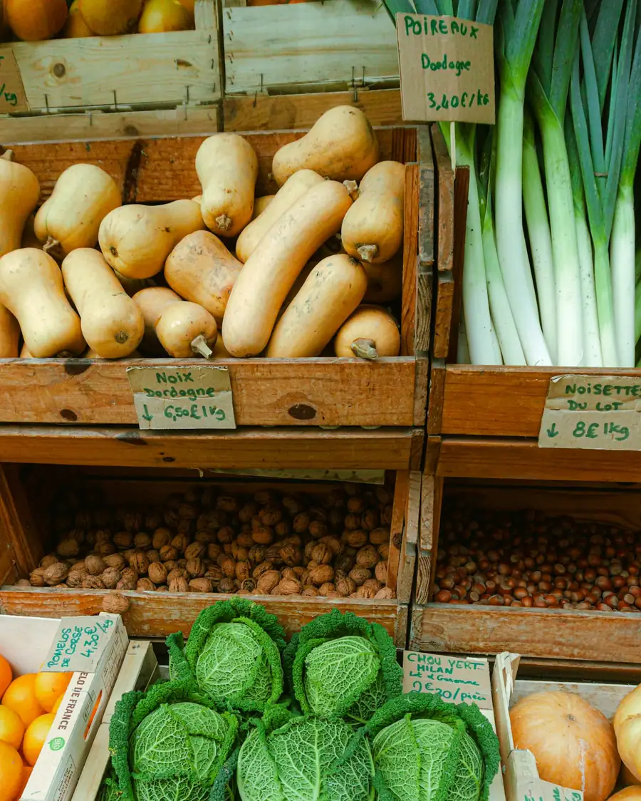 Étal de primeur : cagettes de courges, poireaux, noix, noisettes et choux, avec des étiquettes de prix écrites à la main