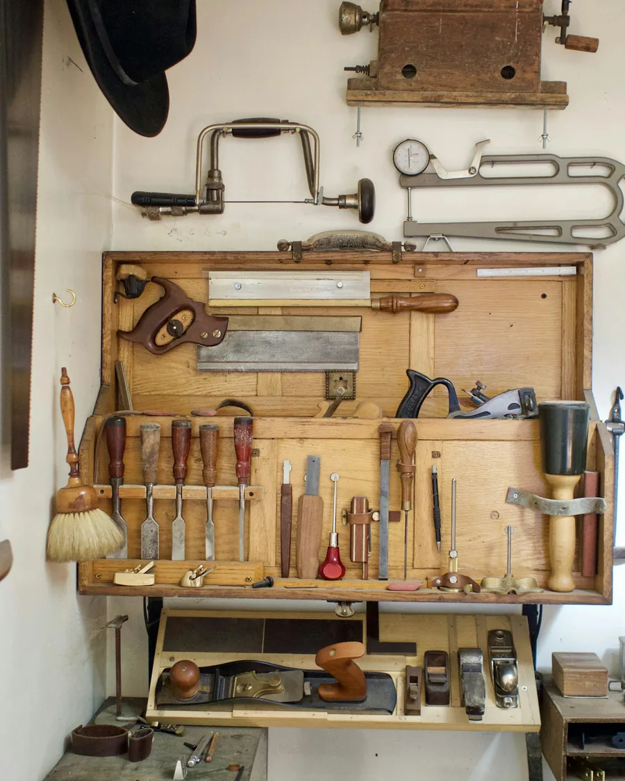 Panneau d'atelier en bois où sont rangés ciseaux à bois, scies, rabots et pinceaux, au-dessus d'un établi