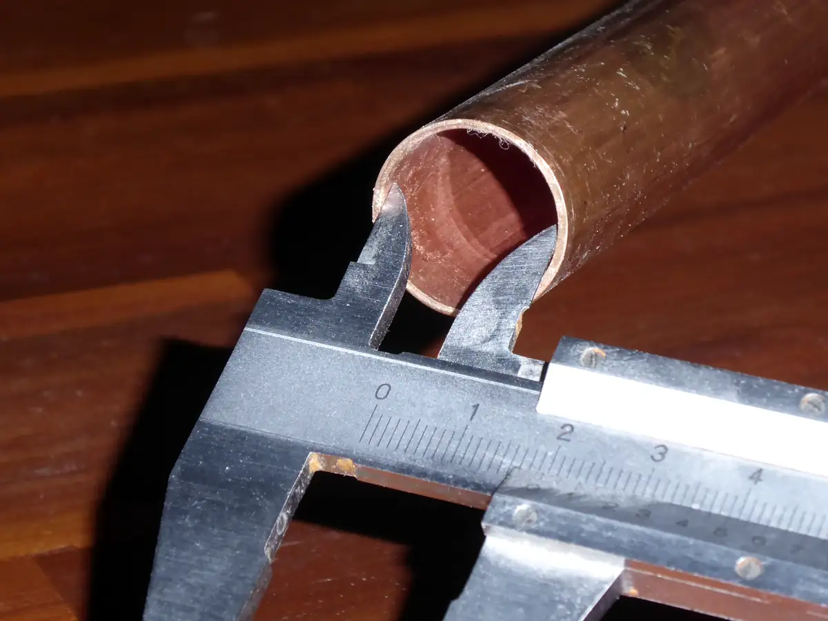 Tube de cuivre coupé net, dont le diamètre intérieur est mesuré au pied à coulisse.