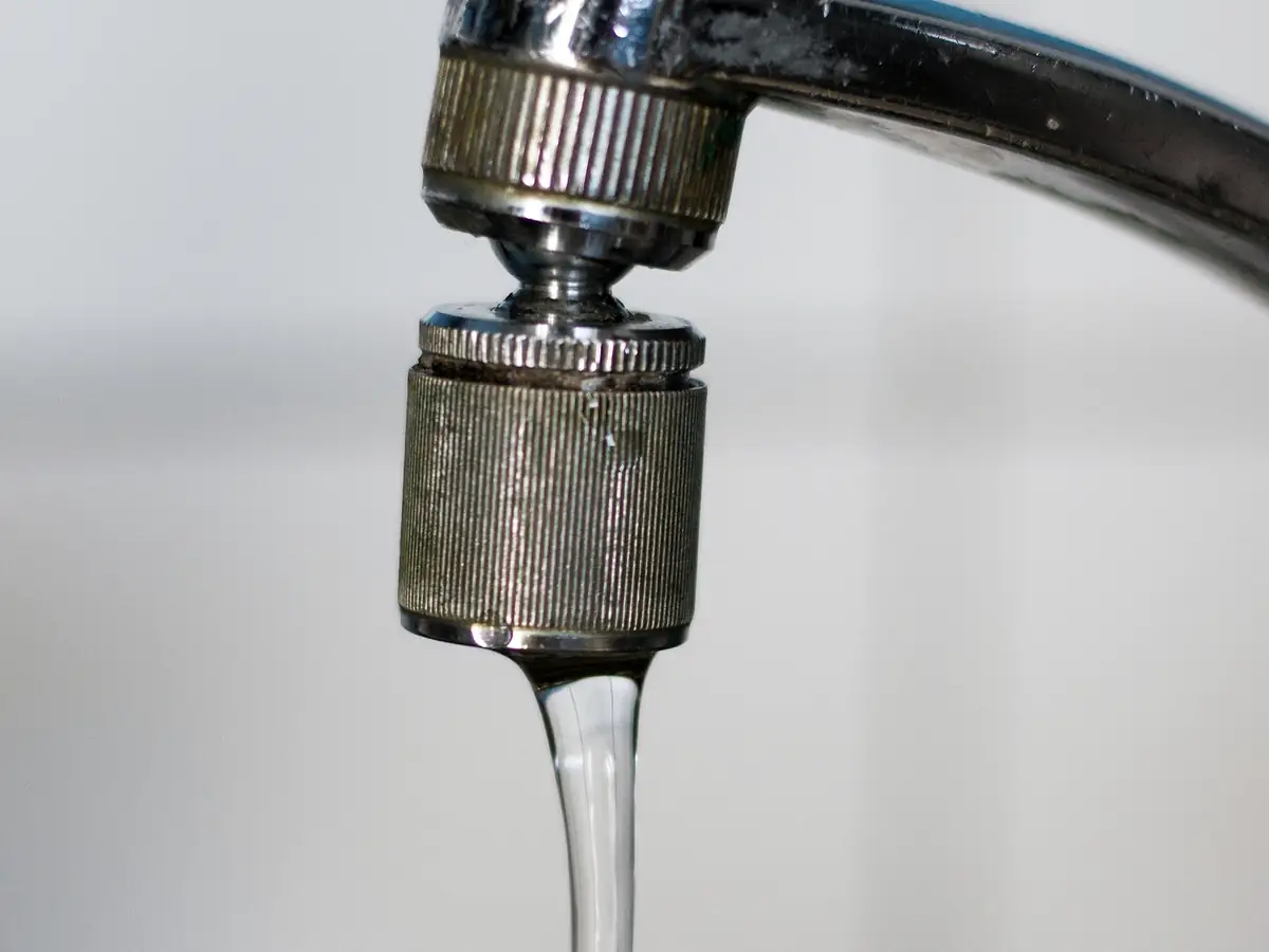 Gros plan sur un mousseur de robinet d'où s'échappe un mince filet d'eau.