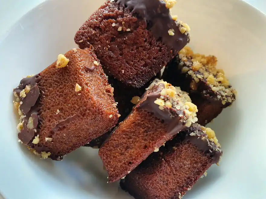 Des parts de gâteau au chocolat nappées et parsemées d'éclats, sur une assiette blanche.