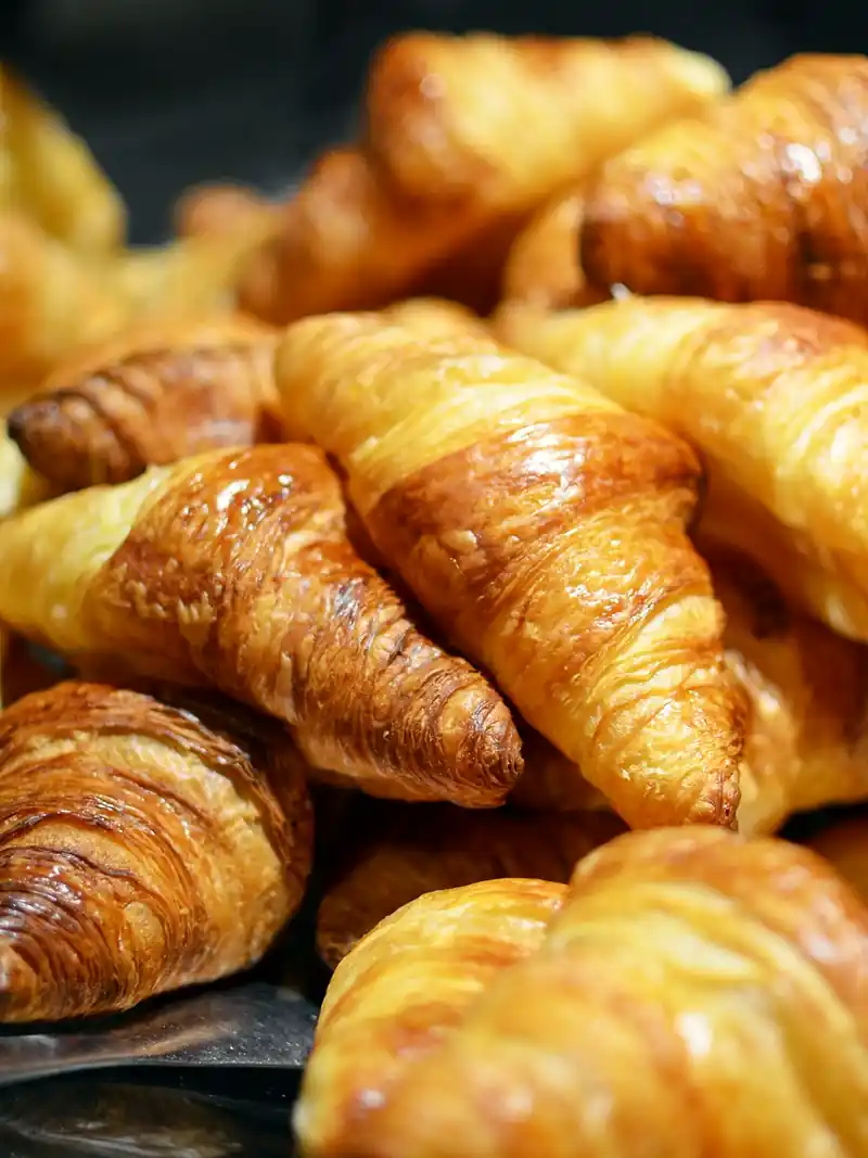 Un tas de croissants dorés et brillants, empilés sur une plaque.