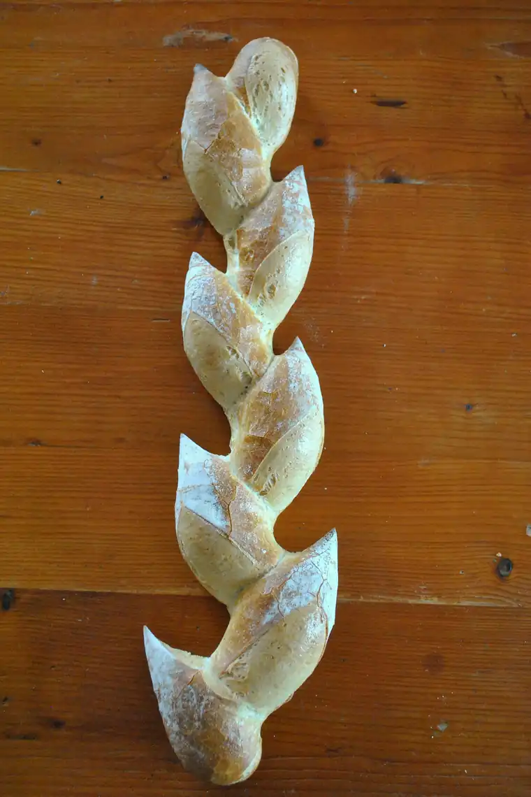 Une baguette en épi crue, façonnée aux ciseaux, posée sur un plan de travail en bois.