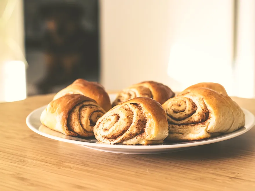 Des roulés à la cannelle dorés, posés sur une assiette blanche à contre-jour.