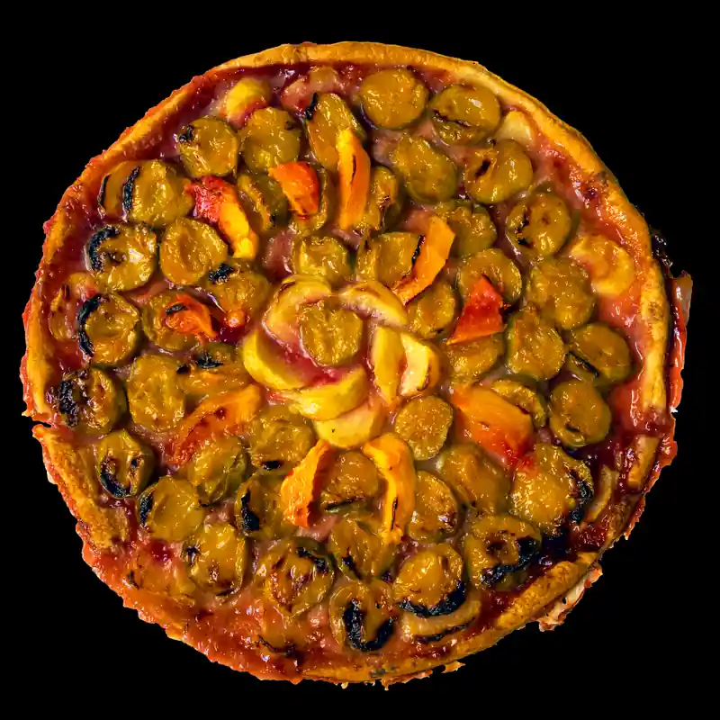 Une grande tarte ronde couverte de petits fruits jaunes caramélisés, sur fond noir.